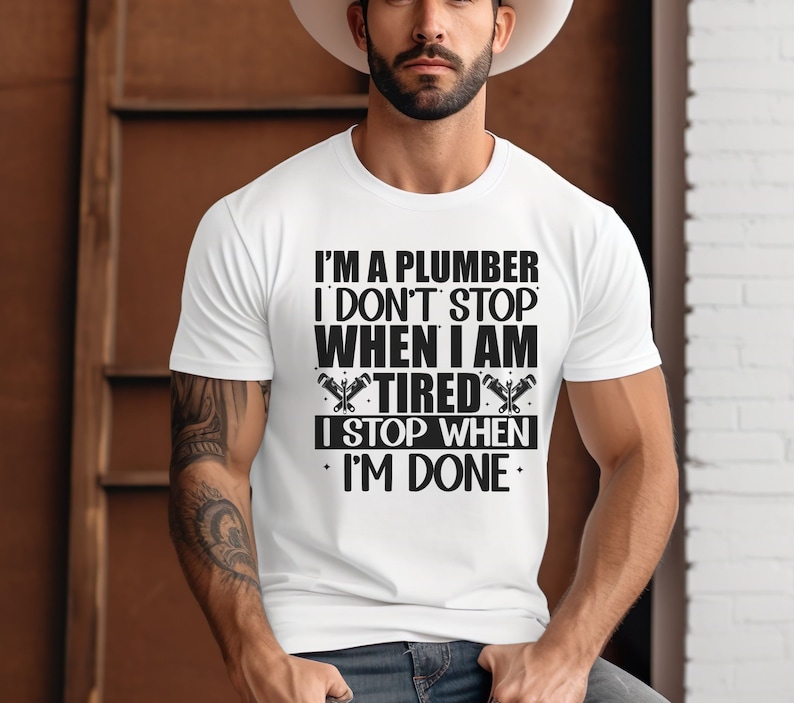 May include: White t-shirt with a black graphic that reads "I'm a plumber I don't stop when I am tired I stop when I'm done".