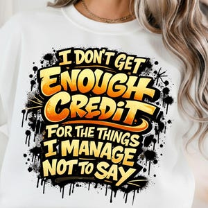 Pu&ograve; includere: Felpa bianca con la scritta "I DON'T GET ENOUGH CREDIT FOR THE THINGS I MANAGE NOT TO SAY" in giallo e arancione, con schizzi e gocce neri.