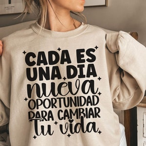 May include: Beige sweatshirt with black text that reads "Cada es una dia nueva oportunidad para cambiar tu vida".