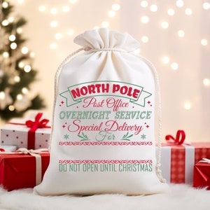 May include: White canvas gift bag with red and green text that reads "North Pole Post Office Overnight Service Special Delivery For" and "Do Not Open Until Christmas".