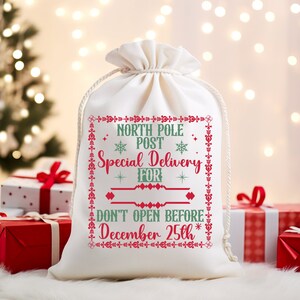 May include: White canvas gift bag with red and green embroidery. The bag says "North Pole Post Special Delivery For Don't Open Before December 25th".