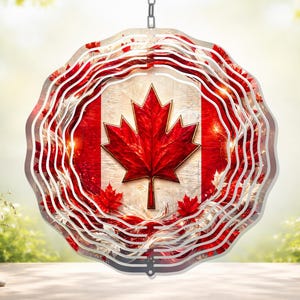 May include: A decorative wind spinner featuring the Canadian flag with a red maple leaf on a white and red background. The spinner has a wavy, layered design and hangs from a chain. The background is a blurred outdoor scene.