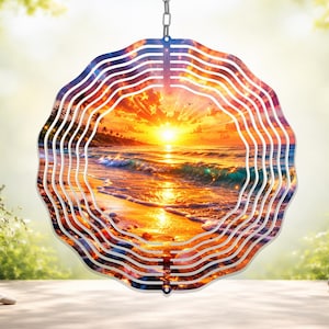 May include: A circular metal wind spinner featuring a vibrant sunset over an ocean beach with waves crashing on the sand. The design consists of concentric scalloped rings that create a layered effect, suspended by a silver metal chain.