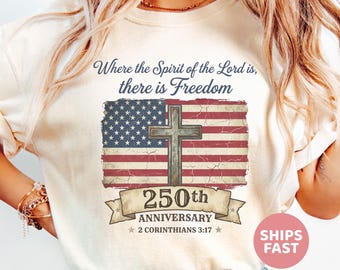 May include: A cream-coloured t-shirt with a distressed American flag design and a cross. The text says "Where the Spirit of the Lord is, there is Freedom" and "250th Anniversary 2 Corinthians 3:17".