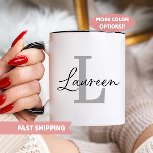 May include: White ceramic mug with a black rim and handle. The mug has a gray letter L and the name "Lauren" written in black cursive script.