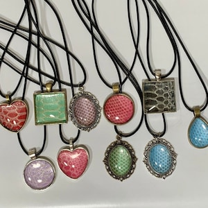May include: Assortment of 10 necklaces with various pendant shapes and designs. The pendants feature a variety of colors and patterns, including green, blue, pink, and white. The necklaces are all made with black cord.