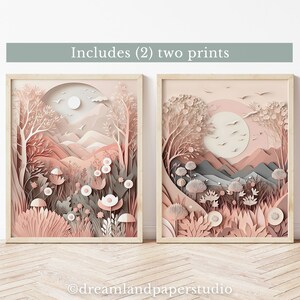 Puede incluir: Dos impresiones de arte de papel cortado enmarcadas en un esquema de color rosa y gris. Las impresiones representan un paisaje con montañas, árboles y flores. El texto "Incluye (2) dos impresiones" está en la parte superior de la imagen.
