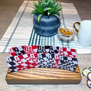 May include: A wooden card holder with a set of playing cards featuring a black and white checkered pattern with red hearts and clubs. The cards are arranged in a fan shape and are sitting on a wooden surface.