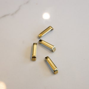 May include: Four gold-colored metal drawer pulls with a rectangular shape and rounded edges.