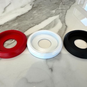 May include: Three circular objects in red, white, and black. Each has a raised outer rim and a central hole. The objects are arranged in a row on a marble-patterned surface. The objects appear to be made of plastic.