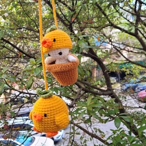 May include: Two crocheted hanging ornaments shaped like chicks in yellow and orange. The chicks are in pots and have small faces.