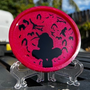 May include: A pink glitter resin coaster with a black silhouette of a person and a flock of birds. The coaster is on a clear plastic stand.