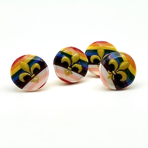 May include: Four round, colorful buttons with a gold fleur-de-lis design. The buttons have a rainbow stripe pattern with a white background.