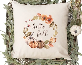 May include: A beige throw pillow with a watercolor design of a fall wreath with pumpkins, leaves, and berries. The wreath has the text "hello fall" in the center.