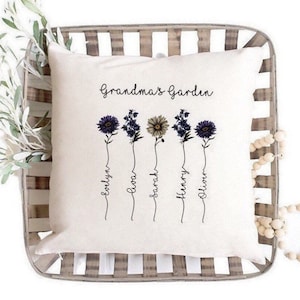 May include: A white throw pillow with the text "Grandma's Garden" printed on it. Five stylised flowers with names written underneath them: Evelyn, Ava, Sarah, Henry, Oliver.