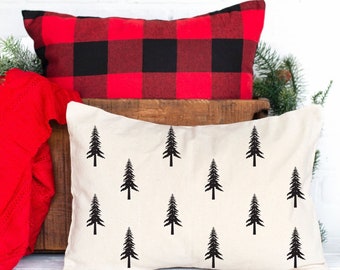 Puede incluir: Una almohada blanca con una silueta negra de pinos repetida en la parte delantera. La almohada está encima de una almohada de cuadros rojos y negros.
