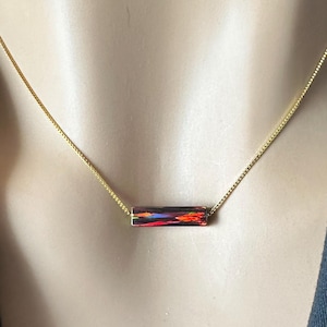 May include: A gold chain necklace with a red, orange, and yellow iridescent bar pendant.