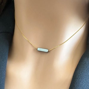 May include: A delicate gold chain necklace with a small, rectangular pendant. The pendant is a light blue colour.