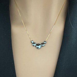 May include: A gold chain necklace with five black and white round stones.