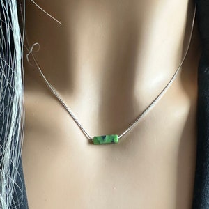 Könnte beinhalten: Eine silberne Kettenkette mit einem grünen Edelstein-Bar-Anhänger.