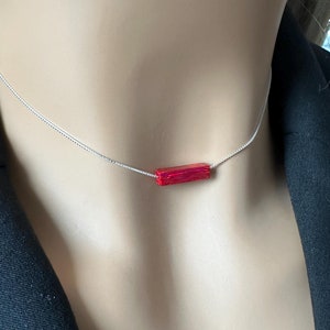 May include: A silver chain necklace with a single, rectangular, red pendant.