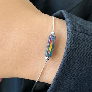 May include: A silver chain bracelet with a single iridescent rectangular bead. The bead has a dark background with streaks of red, yellow, and green.