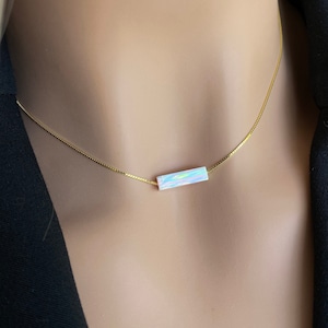 May include: A delicate gold chain necklace with a rectangular iridescent opal pendant.