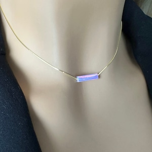May include: A delicate gold chain necklace with a small rectangular pendant. The pendant is made of pink and purple iridescent material.