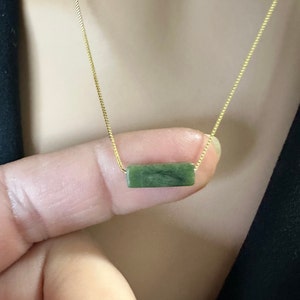 Könnte beinhalten: Eine goldene Kettenkette mit einem rechteckigen grünen Anhänger.