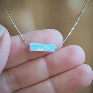 May include: A silver chain necklace with a rectangular opal pendant. The opal is iridescent with shades of blue, green, and pink.