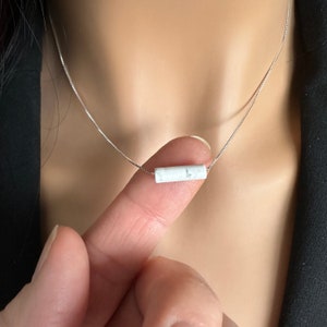 May include: A silver chain necklace with a white marble bar pendant.