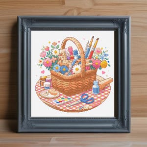 May include: A wicker picnic basket filled with art supplies, including paintbrushes, paint tubes, and a small jar of paint. The basket is surrounded by a colorful bouquet of flowers and is sitting on a checkered picnic blanket.