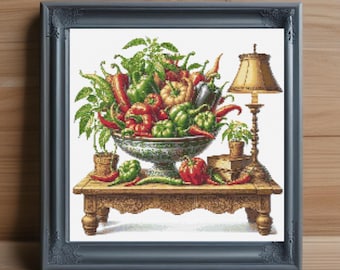 Può includere: Un'opera d'arte a punto croce incorniciata raffigurante una natura morta di peperoni colorati in una ciotola decorativa. I peperoni sono rossi, verdi e gialli, con fogliame verde. Una piccola lampada e piante in vaso sono su un tavolo di legno.