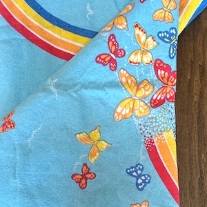 May include: A blue fabric tablecloth with a rainbow arc and a pattern of colorful butterflies. The tablecloth has a white border.