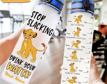 May include: A clear plastic water bottle with a blue lid and a motivational quote that says "Stop Slacking Drink Your Water". The bottle has a cartoon lion on it and a time-based scale with motivational messages like "Get Started", "Remember Your Goal", "Keep Chugging", "Don't Give Up", "Almost There", and "You Did It".