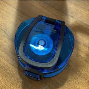 May include: A blue and black water bottle lid with a flip-top lid. The lid has a clear plastic window that shows the inside of the bottle.