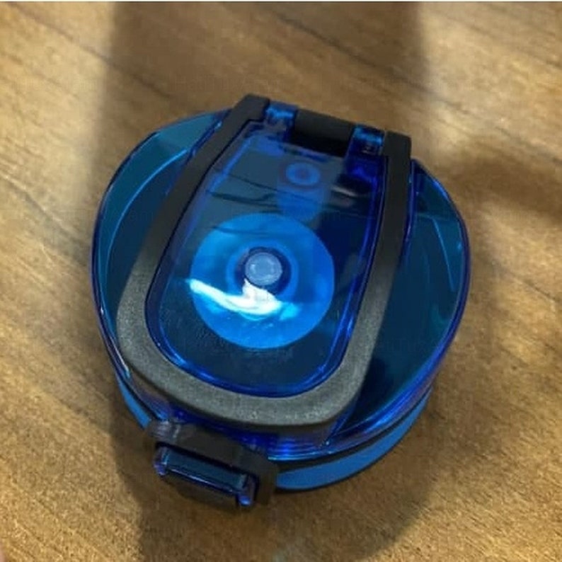 May include: A blue and black water bottle lid with a flip-top lid. The lid has a clear plastic window that shows the inside of the bottle.