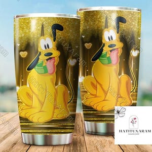 Peut inclure: Un gobelet en acier inoxydable avec un fond de paillettes dorées et une image de dessin animé de Pluto, un chien jaune avec une écharpe verte, en position assise. Le gobelet a un couvercle noir et une poignée noire.