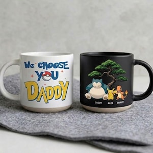 May include: Two ceramic mugs. One white mug with the text "We Choose You Daddy" and a Pokémon design. The other is black, featuring a Snorlax, Pikachu, and Charmander design with the names "Daddy, Alex, Grace".