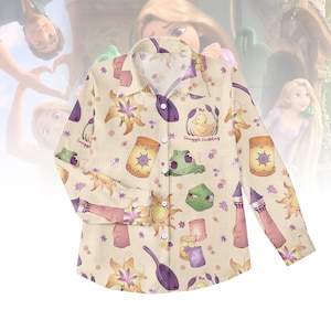 May include: A button-down shirt with a beige background and a repeating pattern of purple, yellow, and pink illustrations. The illustrations include suns, lanterns, flowers, and the text "Snuggle Duckling".