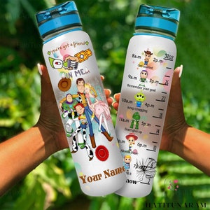 May include: A white water bottle with a blue lid and a Toy Story theme. The bottle has a quote that says "You're got a friend in me." and features characters from the movie. The bottle also has a motivational time tracker with times from 8 a.m. to 7 p.m. and a measurement scale up to 900 ml.