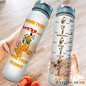 Puede incluir: Una botella de agua blanca con una tapa azul y un diseño de perro de dibujos animados. La botella tiene una cita motivacional que dice "Bebe tu agua y ocúpate de tus asuntos". La botella también tiene un rastreador de tiempo con un diseño de perro de dibujos animados para cada hora.