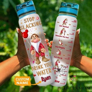 Puede incluir: Una botella de agua transparente con una tapa azul y una cita motivacional que dice "Stop Slacking Drink You Water". La botella tiene un gráfico de un enano de dibujos animados con un sombrero rojo y una camisa roja y blanca. La botella también tiene un rastreador de citas motivacionales con un gráfico de enano de dibujos animados para cada cita. Las citas son "Get Started", "Remember Your Goal", "Keep Chugging", "Don't Give Up". La botella tiene un nombre personalizado "Ryan" impreso en ella.