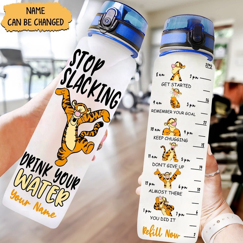 May include: A clear plastic water bottle with a blue lid and a motivational quote that says "Stop Slacking Drink Your Water Your Name". The bottle has a cartoon image of a tiger on it and a time-based water intake tracker with a cartoon tiger image for each time.
