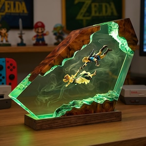 May include: A decorative resin and wood lamp featuring two miniature figures suspended in a translucent green, smoke-filled interior. The figures are reaching towards each other, encased within a jagged, polished wood frame on a rectangular base.