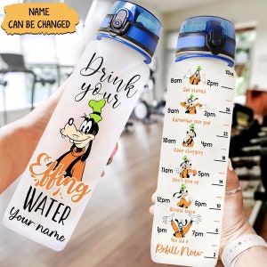 Op de afbeelding: Een doorzichtige plastic waterfles met een blauwe dop en een cartoonafbeelding van Goofy. De fles heeft een motiverende quote die zegt "Drink your Effing Water" en een tijdtracker met Goofy-afbeeldingen. De fles is 32 ounce.