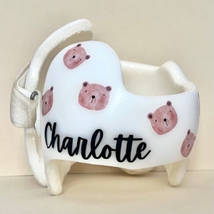 May include: White helmet with a personalized name "Charlotte" in black cursive lettering. The helmet is decorated with multiple brown bear stickers with pink accents.