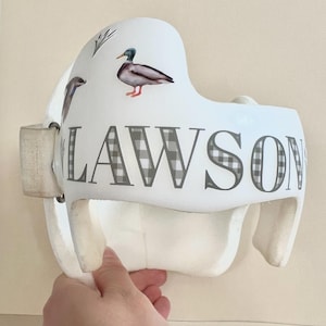 May include: White helmet with a black and white checkered pattern and the name "LAWSON" printed on it. The helmet has a duck and other bird designs.