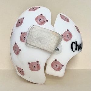 May include: White helmet with a brown bear pattern and the name "Charlie" written in black on the side. The helmet has a white strap with a velcro closure.