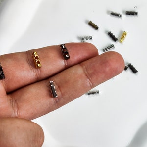 Könnte beinhalten: Sortiment an Metall-Schnallenenden in Gold, Silber und Schwarz. Die Schnallenenden haben drei Löcher und werden zum Befestigen von Schnüren oder Bändern verwendet.